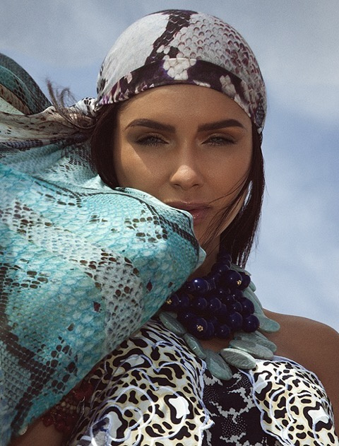 Close-up of Jamillette Gaxiola in a snakeskin-print headscarf looking at the camera, a turquoise snakeskin-print scarf blowing across her chin, with a dark blue bead necklace and animal-print top.